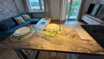 En matplats med ett bord i marmor, en soffa och en tv i en modern lägenhet med stora fönster.