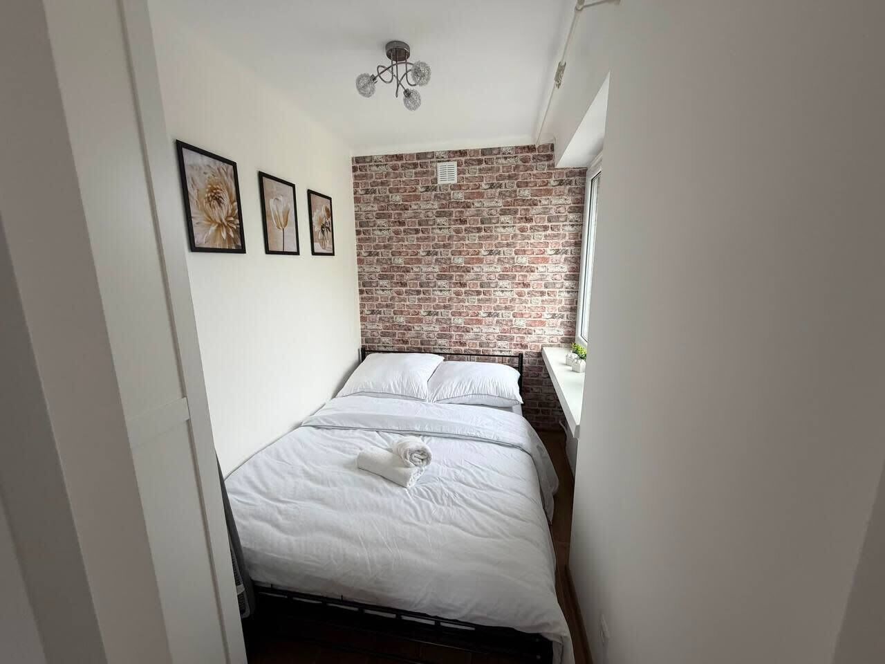 Un dormitorio con pared de ladrillo, cama con ropa blanca y una ventana.