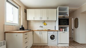 Pieni, käytännöllinen keittiö, jossa on valkoiset kaapit, pesukone ja ikkuna.