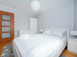 A bedroom with a bed, a wardrobe, a bedside table, and a door with frosted glass panels. - Piotrkowska Spacious Apartment (Łódź)