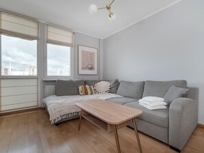 A modern living room with a grey sofa, a wooden coffee table, and a city view through large windows. - Piotrkowska Spacious Apartment (Łódź)