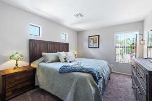A bedroom with a bed, nightstand, dresser, and a window with a view.