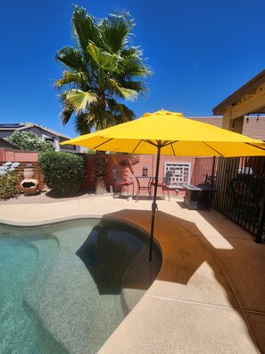 A swimming pool with a yellow umbrella, a palm tree, and outdoor furniture.