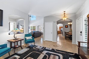 A spacious living area with a sofa, armchairs, a coffee table, and a rug. There is a dining area with a table and chairs, and a kitchen in the background.