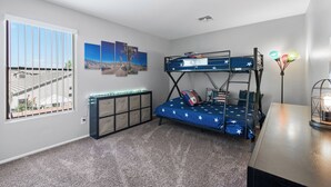 Ein Stockbett mit einem Bettbezug mit Sternenmuster, ein Schreibtisch mit Lampe und ein Fenster mit Jalousien.