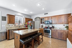 A kitchen with wooden cabinets, stainless steel appliances, a granite countertop, and a central island with bar stools.