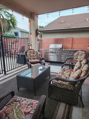 An outdoor patio with wicker furniture, a glass-top table, and a barbecue grill.