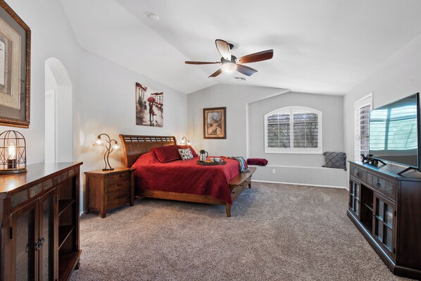 A bedroom with a bed, a ceiling fan, a window, and a TV.