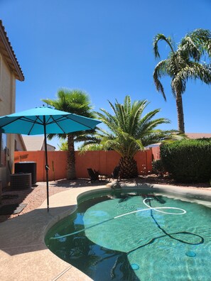 A swimming pool with clear water, surrounded by palm trees and a blue umbrella.