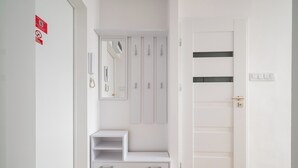 A white hallway with a door, a coat rack, a mirror, and a telephone. - Park Mirowski Central Apartment (Warszawa)