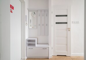 A white hallway with a door, a coat rack, a mirror, and a telephone. - Park Mirowski Central Apartment (Warszawa)