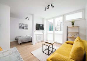 Un salon moderne avec un lit, un téléviseur, un canapé jaune et une plante.