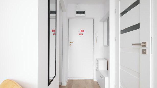A hallway with a white door, a wall-mounted phone, and a shelf unit. - Park Mirowski Central Apartment (Warszawa)