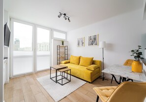 A modern living room with a sofa, coffee table, and dining table, large windows, and a city view. - Park Mirowski Central Apartment (Warszawa)