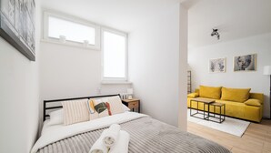 A bedroom with a bed, a nightstand, a bedside table, a yellow sofa, and a window. - Park Mirowski Central Apartment (Warszawa)