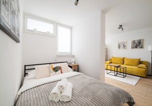 A bedroom with a bed, a nightstand, a bedside table, a yellow sofa, and a window. - Park Mirowski Central Apartment (Warszawa)