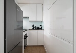 A compact kitchen with white cabinets, a stainless steel refrigerator, and a built-in oven. - Park Mirowski Central Apartment (Warszawa)