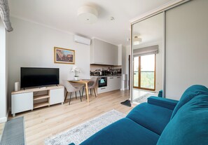 A modern living room with a flat-screen TV, a sofa, a dining area with a table and chairs, and a kitchen in the background. - Pawia Studio Centrum 70 (Warszawa)