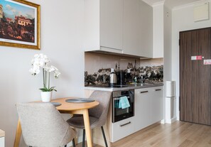 A modern kitchen with a dining area, featuring a painting, orchid flowers, and a view of a cityscape. - Pawia Studio Centrum 70 (Warszawa)