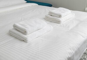 Een net opgemaakt bed met witte lakens en twee opgevouwen handdoeken aan de zijkant.