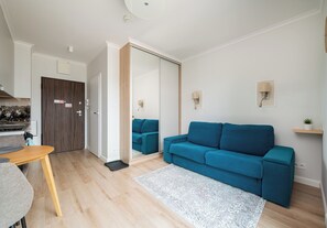 A modern living room with a blue sofa, a wooden dining table, and a kitchen area with a wooden door. - Pawia Studio Centrum 70 (Warszawa)
