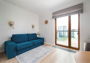 Een moderne woonkamer met een blauwe bank, een vloerkleed met dessin en een uitzicht op gebouwen door een groot raam met gordijn.