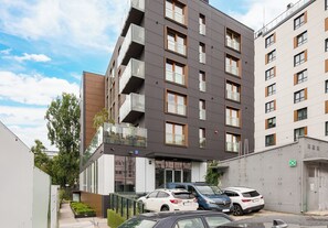 A multi-story building with balconies, a parking area with cars, and a clear sky. - Pawia Studio Centrum 70 (Warszawa)