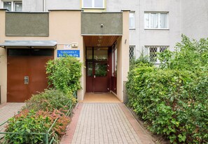 A building entrance with a brown door, a signboard, and a paved pathway leading to the entrance. - Wilanów Comfort Stay Apartment (Warszawa)