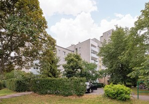 Een woongebouw met meerdere balkons, omgeven door volgroeide bomen en een verzorgd gazon.