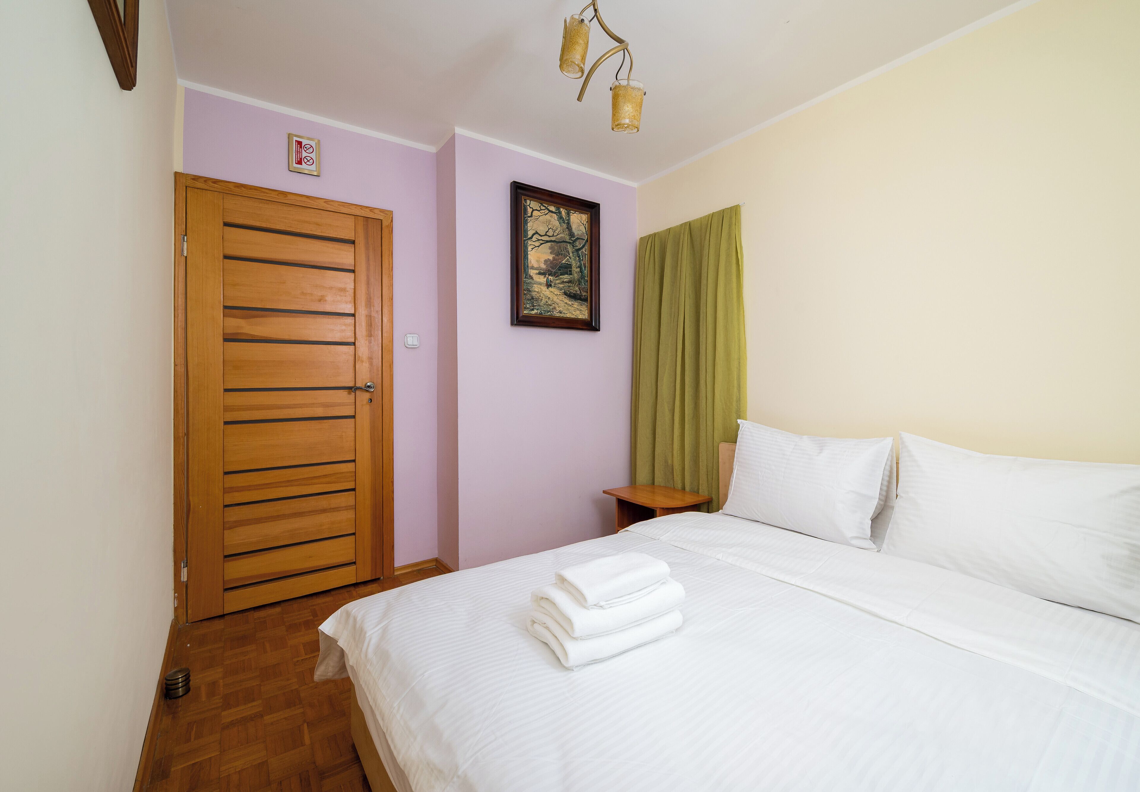 A bedroom with a wooden door, a framed picture on the wall, a bedside table, and a neatly made bed.