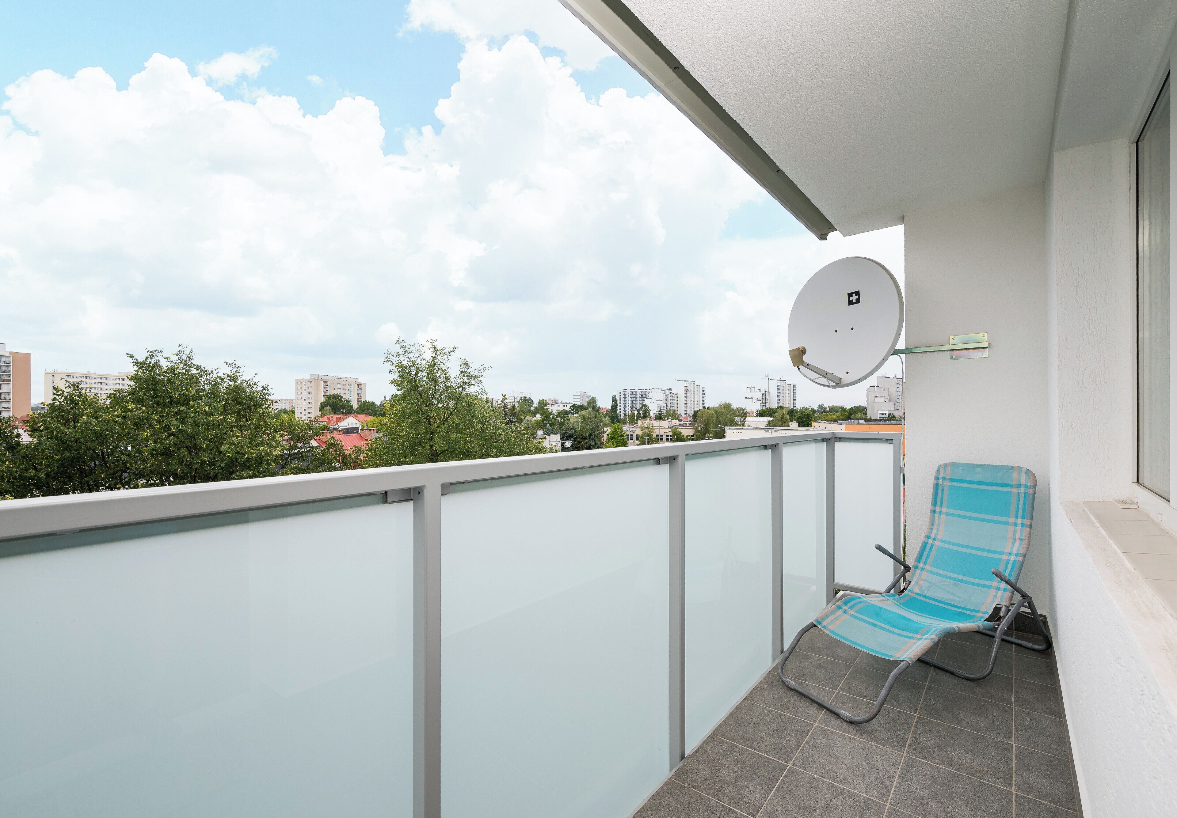 A balcony with a glass railing, a blue chair, and a satellite dish.
