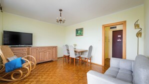 A living room with a sofa, a television, a dining table with chairs, a wooden cabinet, and a chandelier. - Wilanów Comfort Stay Apartment (Warszawa)