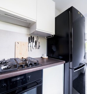 Una cuina moderna amb un frigorífic negre, una cuina de gas i una taula de tall de fusta.