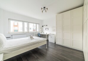 Ein Schlafzimmer mit Bett, Schreibtisch, Stuhl, Kleiderschrank und Fenster.