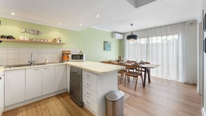 A modern kitchen with white cabinets, a dishwasher, and a microwave. There is a dining area with a table and chairs.