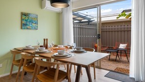 A dining area with a table set for four, a hanging pendant light, and a sliding glass door leading to an outdoor seating area.
