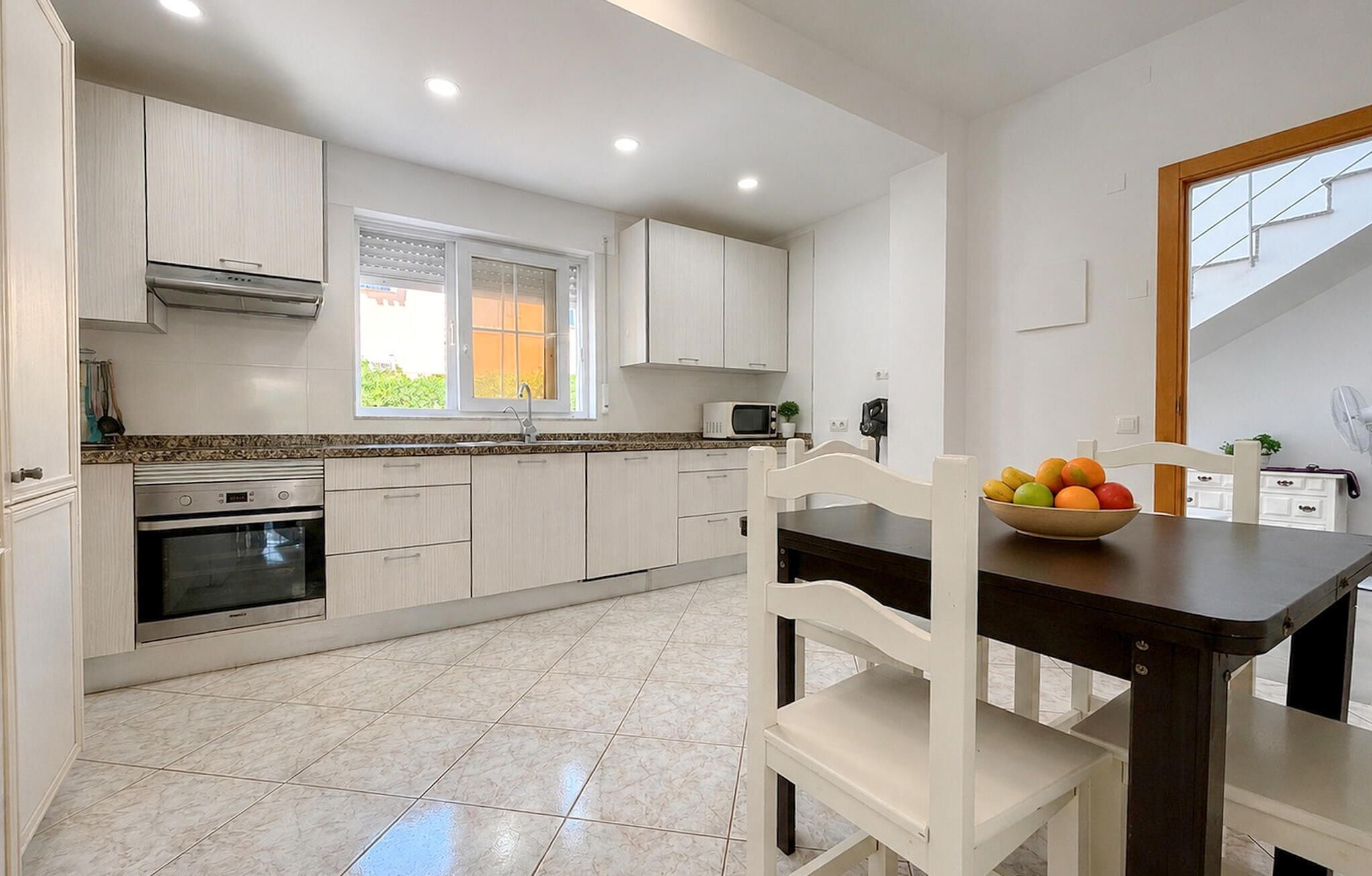 A modern kitchen with white cabinets, a built-in oven, a microwave, and a window.