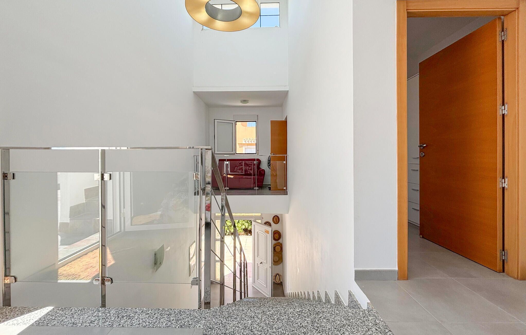 A modern interior with a glass door entrance, a staircase leading to a balcony, and a wooden door.