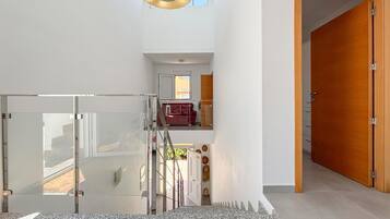 A modern interior with a glass door entrance, a staircase leading to a balcony, and a wooden door.