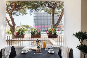 A balcony with a table set for breakfast, potted plants, and a view of a building with a sign. - The City Loft by Riviera Collection (Riccione)