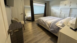Een slaapkamer met een bed, een stoel, een kledingkast, een spiegel en een raam met gordijnen.