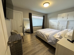 Ein Schlafzimmer mit Bett, Stuhl, Kleiderschrank, Spiegel und einem Fenster mit Vorhängen.