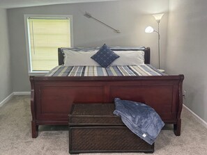 A bedroom with a bed, a nightstand, a lamp, a window with blinds, and a carpeted floor. - Mermaid by the Coast  4BR Near Beach & Refineries (Clute)