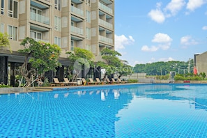 Piscina com espreguiçadeiras e um edifício com varandas ao fundo.