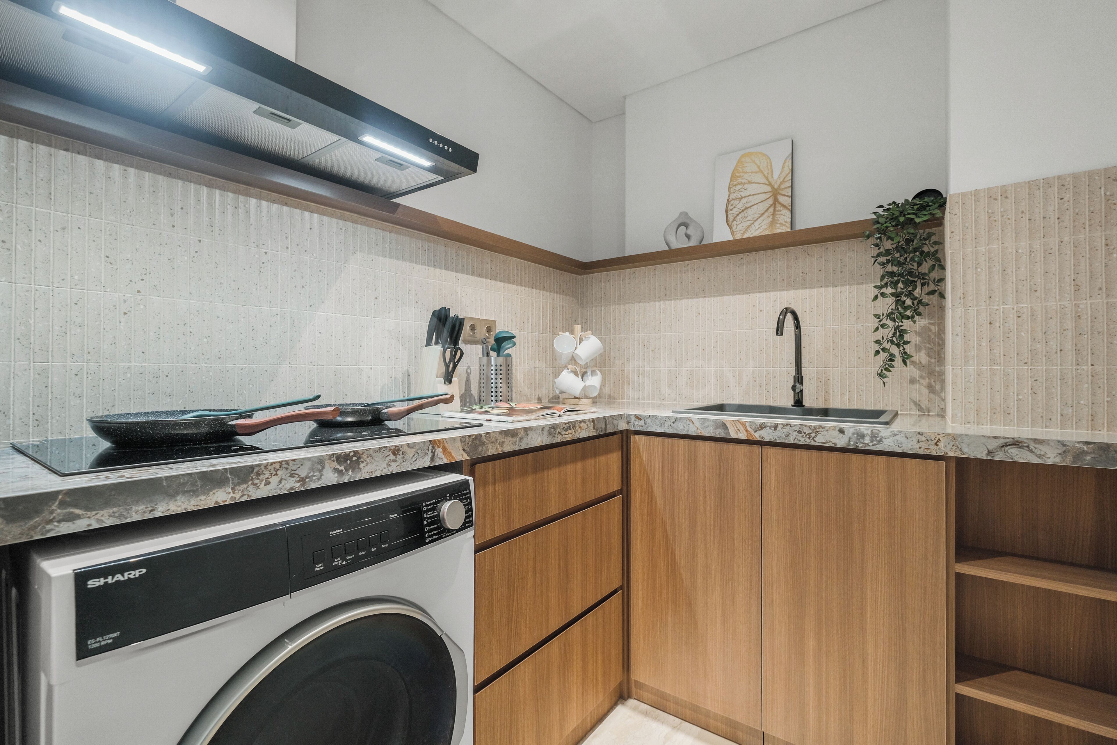Cocina compacta con lavadora, un lavamanos, armarios de madera y una encimera con diversos utensilios de cocina.