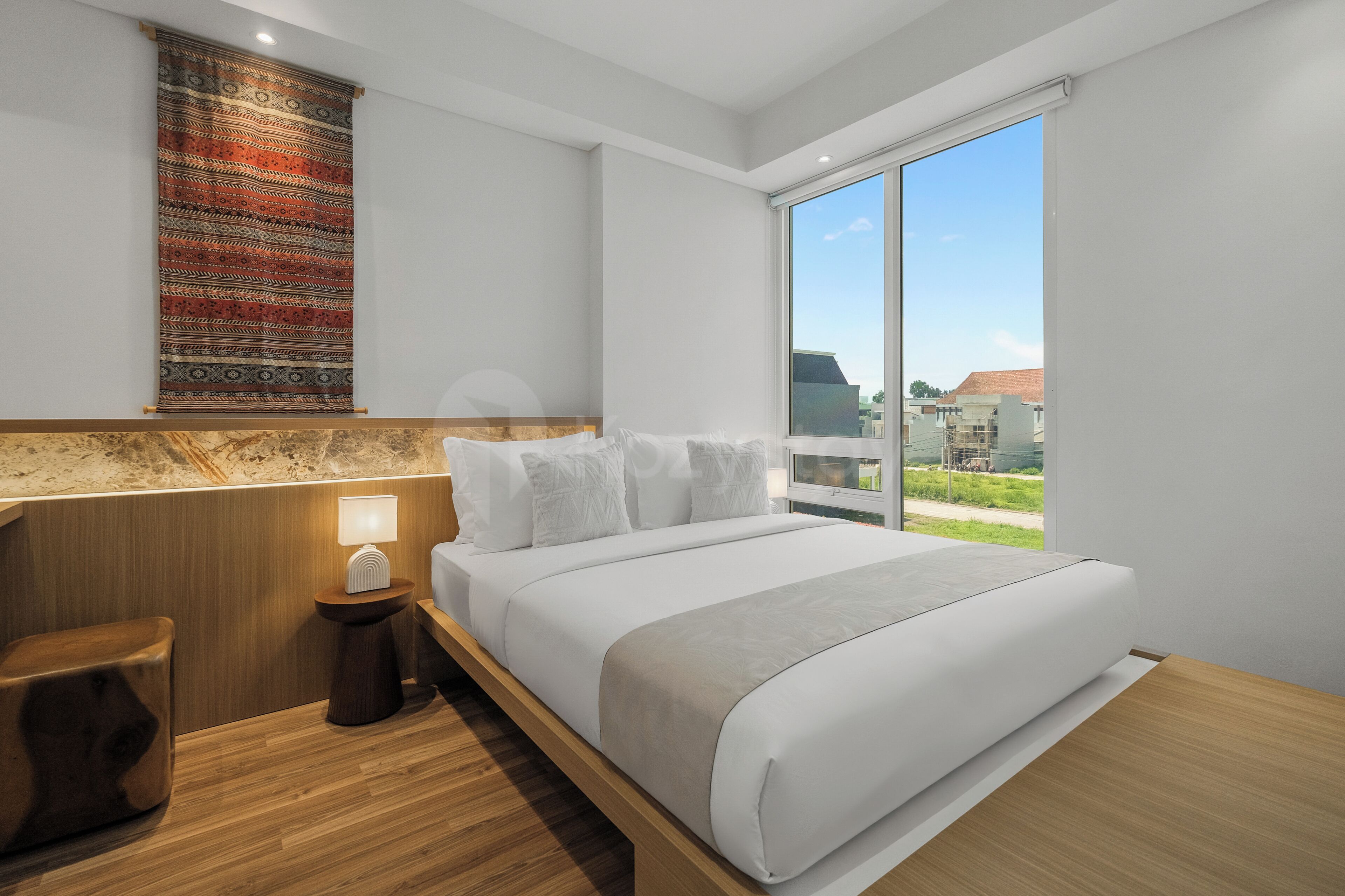 Een moderne hotelkamer met een groot bed, een nachtkastje, een lamp, een houten hoofdeinde en uitzicht op de stad door een groot raam.