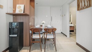 Et moderne spiseområde med et bord dækket til to personer, en vanddispenser og et træskab med dekorative genstande.