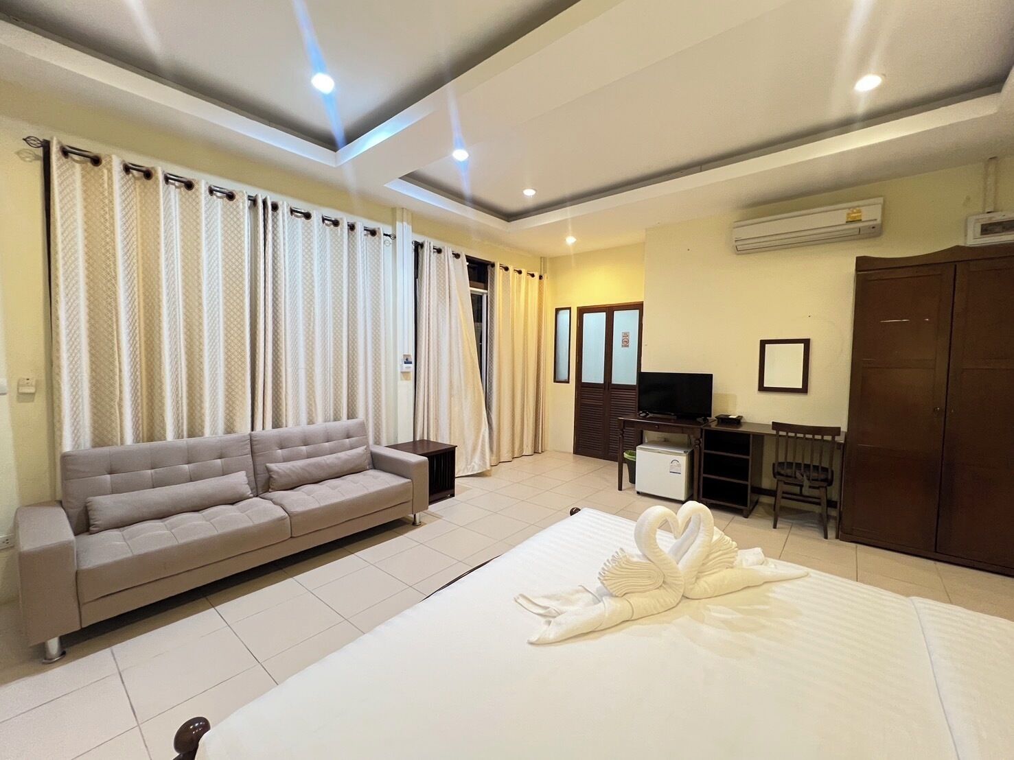 A hotel room with a bed, a sofa, a TV, a small fridge, and a wardrobe.