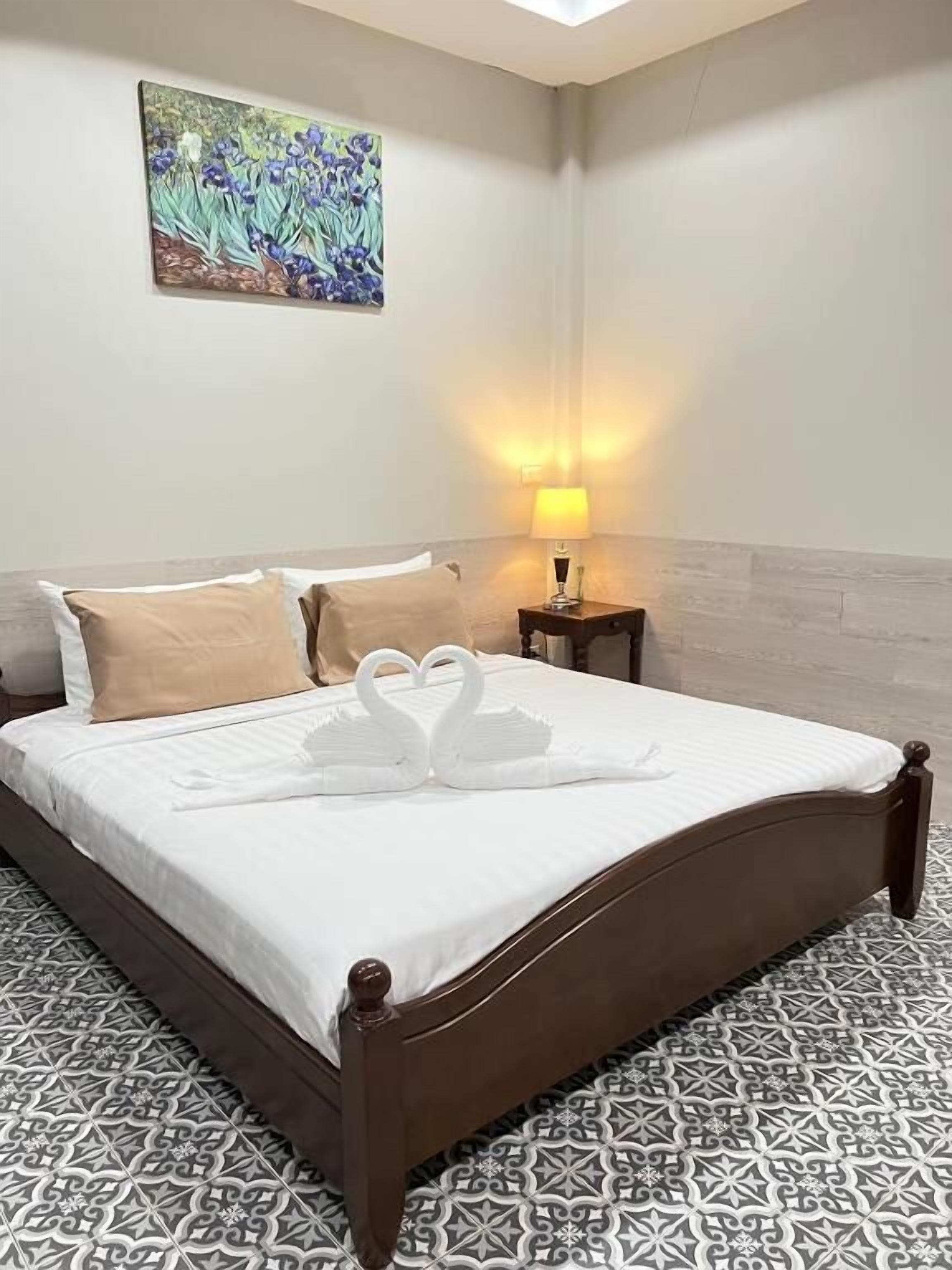 Una habitación de hotel con cama, mesita de noche, lámpara y un cuadro en la pared.