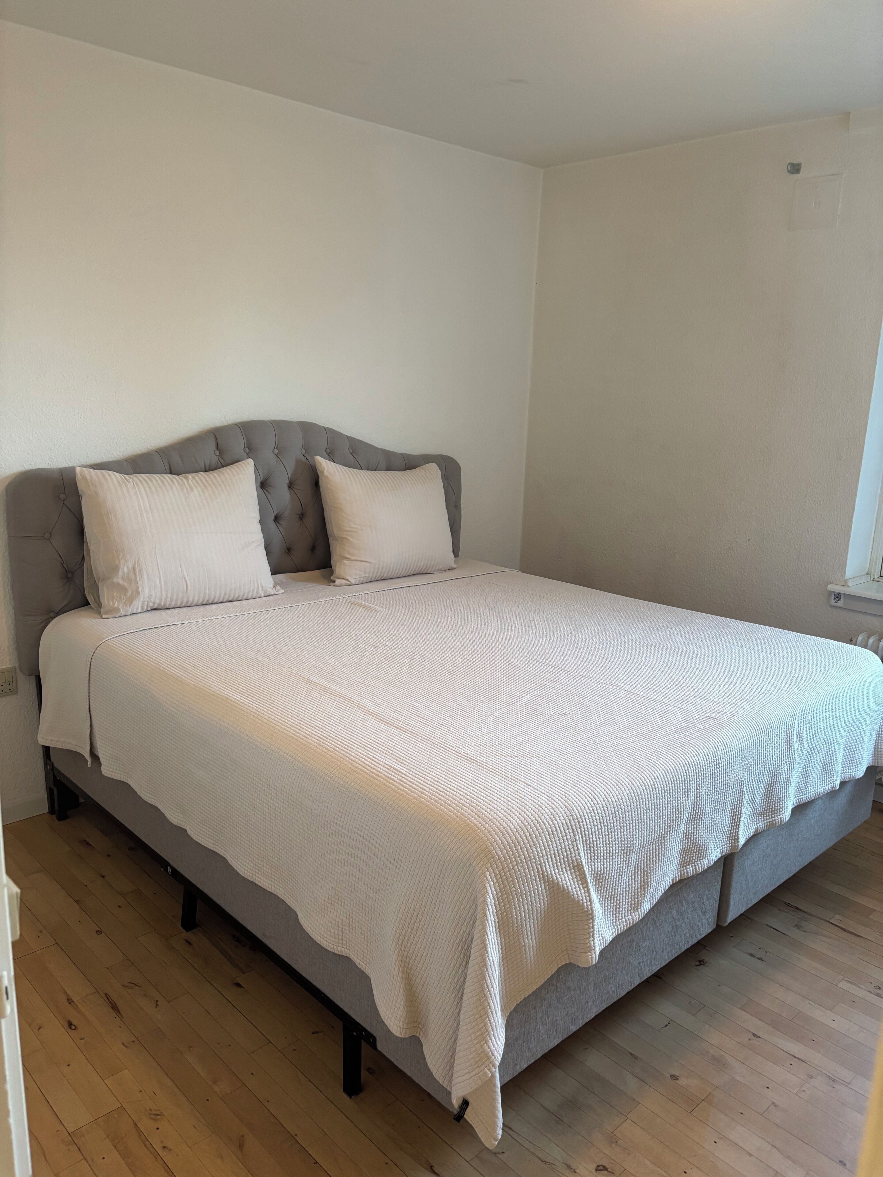 A bedroom with a bed, a grey upholstered headboard, and a white textured bedspread.